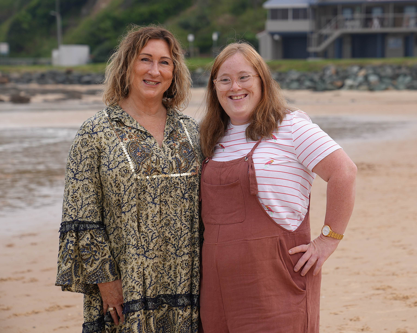 Vicki Smyth, Northcott Taree Service Coordinator with Emma, standing close together and smiling on a beach
