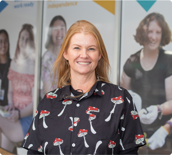 A portrait of a woman with orange hair smiling at the camera. She is wearing a black shirt with red and white mushrooms on it. This is Rachel.
