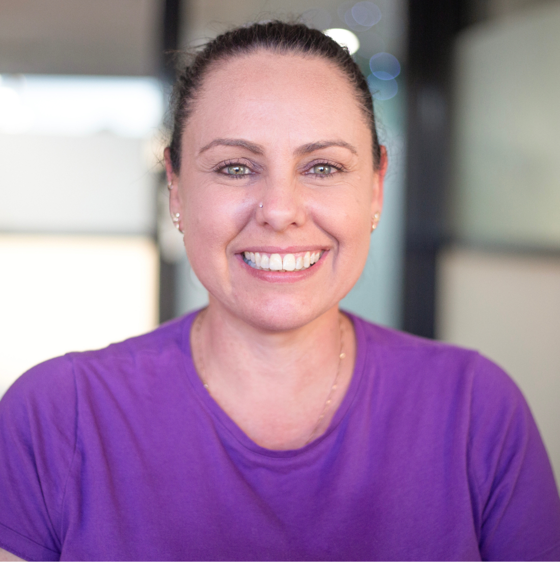 A headshot of a woman looking directly at the camera, smiling, wearing a purple t-shirt.