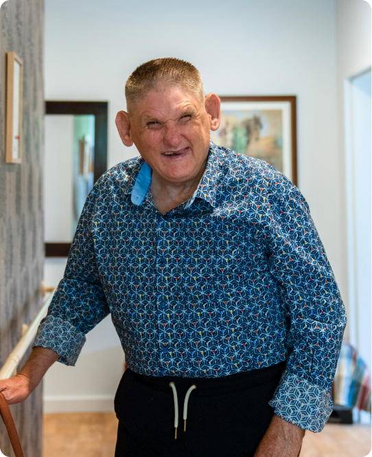 A man in a blue collared shirt and pants is in a hallway, holding a rail. He is smiling. His name is David.