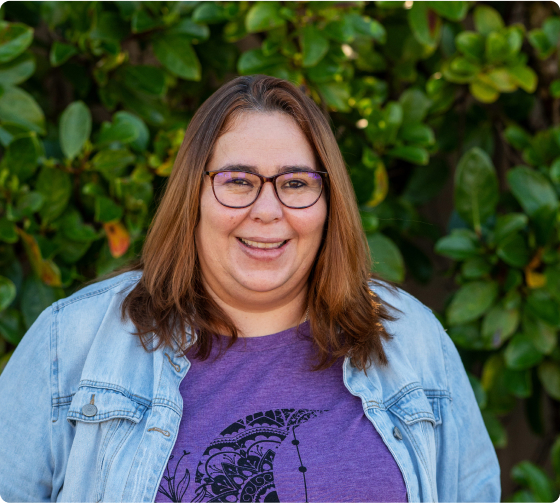 A headshot of a woman wearing a denim overshirt and a purple t-shirt. She is smiling.