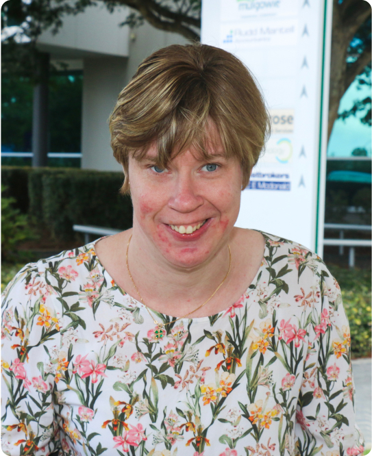 A woman is smiling at the camera. She is wearing a floral top and has short blond hair.